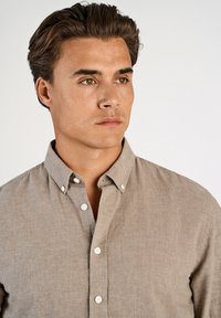 Camicia marrone chiaro con bottoni e collo a camicia, bottoni bianchi; realizzata in tessuto strutturato, con una vestibilità morbida.