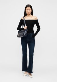 Top nero con spalle scoperte, jeans svasati blu scuro e scarpe bianche a punta. Porta una borsa a tracolla blu navy con dettagli in metallo dorato.