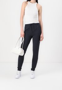 Figurpassande vit ribbad linne, marinblå joggers med dragsko, vit handväska och vita sneakers; mjuk textur och enkel design.