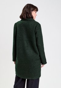 Zielony, futrzasty, oversize'owy płaszcz z kołnierzem i długimi rękawami, z teksturowanej tkaniny, o długości do połowy uda.