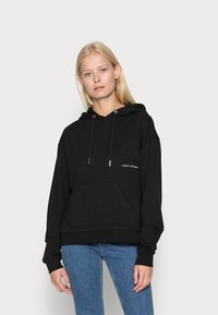 Felpa nera con cappuccio, tasca frontale, chiusura con cordino e logo del marchio. Texture morbida, vestibilità ampia e polsini a coste.