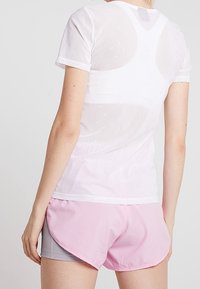 Camiseta atlética blanca, semitranslúcida, de manga corta, con patrones geométricos sutiles; combinada con shorts rosas y grises de dobladillo curvado.
