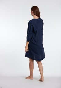 Abito blu navy, lungo fino al ginocchio, con maniche a tre quarti, vestibilità ampia, scollo rotondo e una fessura sul retro, realizzato in tessuto leggero.