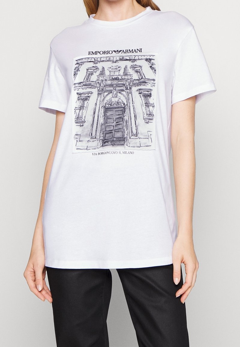 Bílý bavlněný tričko s šedou ilustrací fasády budovy a textem "EMPORIO ARMANI" a "VIA BORGONUOVO 11, MILANO."