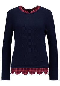 Haut texturé bleu marine à manches longues superposé sur une chemise à carreaux rouges et noirs à ourlet festonné avec un détail de col assorti.