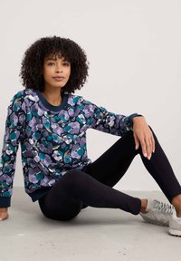 Virágmintás pulóver különböző lila és zöld árnyalatokban, puha anyagból készült, kerek nyakkivágással és bordás mandzsettával, fekete leggingsszel párosítva.