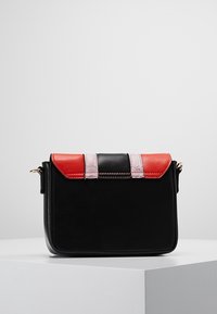 Borsa a mano rettangolare nera con dettagli rossi e rosa sulla pattina, esposta su un piedistallo bianco su uno sfondo semplice.