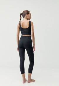 Čierne rebrované legíny a zodpovedajúci crop top, ktorý má výstrih do oblúka a nízky chrbát, s textúrovaným povrchom a minimálnymi kovovými detailmi.