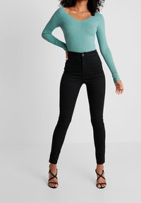 Długi rękaw, prążkowany bodysuit w miętowym kolorze z dekoltem w serek, zestawiony z czarnymi, wysokogatunkowymi jeansami skinny i czarnymi sandałami na ramiączkach.