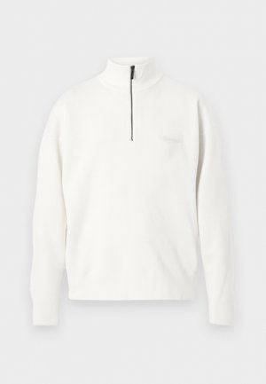 Λευκό πουλόβερ με μακριά μανίκια, ψηλό γιακά και μερικό μαύρο φερμουάρ στο κέντρο μπροστά.