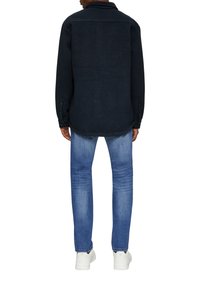 Dunkelblause, gewebte Shirtjacke mit einem kragenförmigen Ausschnitt, geknöpften Manschetten und einem leicht gebogenen Saum, kombiniert mit hellblauen Jeans und weißen Turnschuhen.