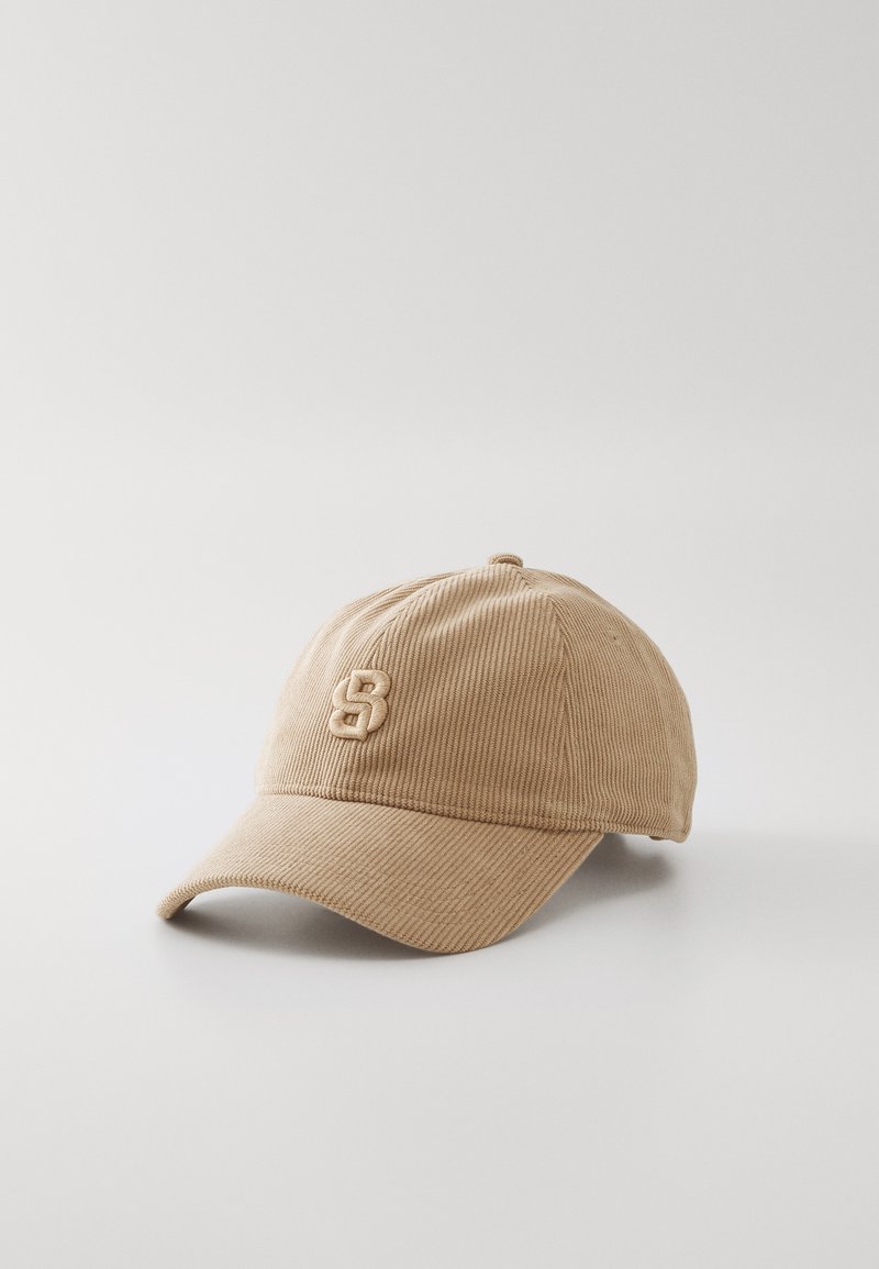 Kaki kordfløyels baseball cap med en avrundet krone, buet skjerm og en brodert logo på forsiden. Har vertikal tekstur gjennom hele.