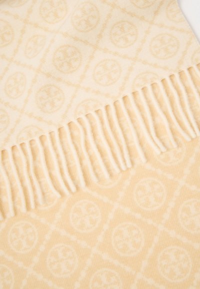 Lichtgekleurde, zachte geweven deken met een ruitenpatroon en cirkelvormige motieven; franjes aan één rand. Gladde textuur.