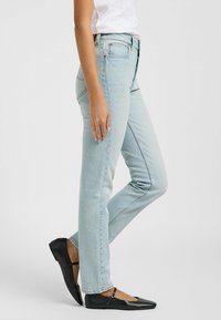 Jeans in denim azzurro chiaro a gamba dritta con cinque tasche, passanti per cintura e una trama sottile, abbinati a ballerine nere con una cinghia.