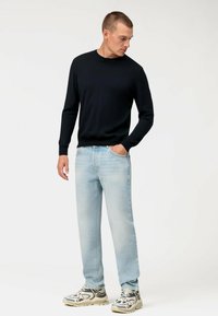 Maglione nero a maniche lunghe, jeans dritti azzurri chiari e sneakers stampate; l'outfit presenta una vestibilità casual e rilassata con dettagli minimi.