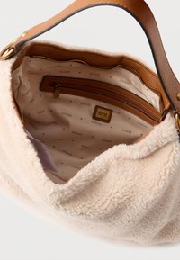 Miękka beżowa torba z fakturowaną futrzaną powierzchnią i gładkim brązowym skórzanym paskiem. Wnętrze zawiera kieszeń na zamek oraz podszewkę z wzorem markowym.