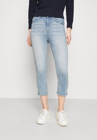 Jeans cortos de color azul claro hechos de denim, con un diseño clásico de cinco bolsillos, ligeras desgastadas y dobladillos desflecados, combinados con zapatillas blancas.
