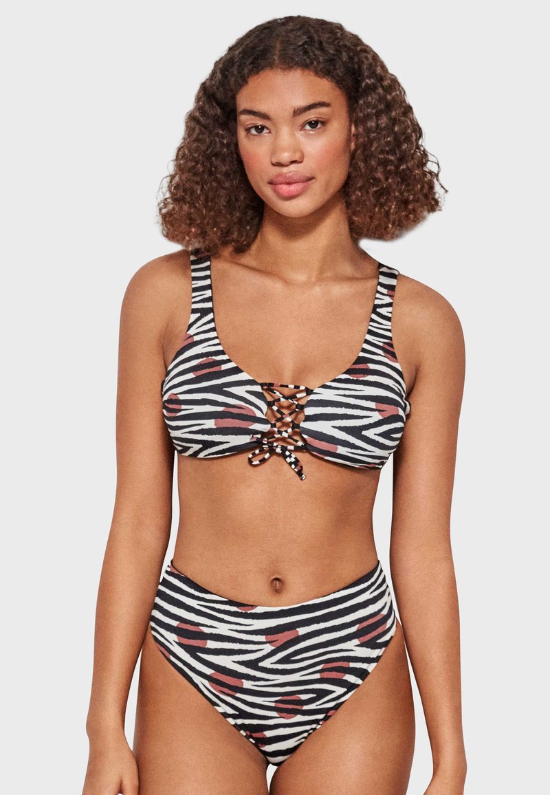 Bikini a rayas en blanco y negro con acentos rojos, que presenta un diseño delantero con cordones y partes inferiores de cintura alta. Textura suave.
