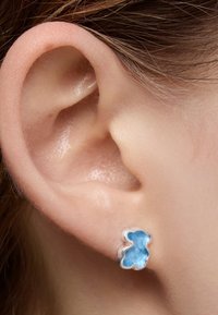 Orecchino a perno a forma di orso d'argento con una finitura in smalto lucido di colore azzurro chiaro, mostrato in primo piano su un orecchio.