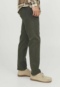 Pantalones rectos de algodón verde oscuro, con un clásico diseño de cinco bolsillos, combinados con unos zapatos de ante beige claro.