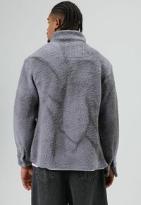 Grijze fleecejas met een textuurrijke, pluizige buitenkant, hoge kraag en verlaagde schouders. Afgewerkt met een losse pasvorm en subtiele naden.