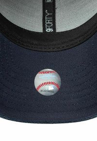 Casquette de baseball bleu marine avec une visière courbée, arborant un autocollant circulaire de la MLB sur le dessous. Design structuré avec un tissu texturé.
