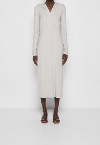 Långärmad, ljusgrå klänning med huva, med en djup v-ringning och en avslappnad passform, kombinerad med bruna sandaler med remmar.