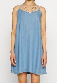 Ljusblå denimklänning med tunna band, V-ringning, enkel design och avslappnad passform. Subtil textur med fåll som slutar ovanför knät.