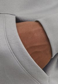 Poche d'un sweatshirt gris à tissu texturé ; main partiellement visible à l'intérieur, montrant le teint de la peau et des coutures détaillées le long du bord.