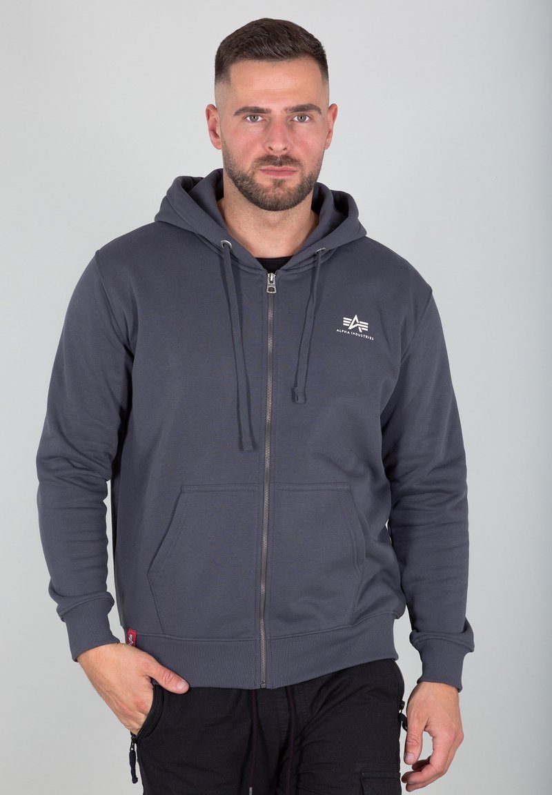 Siva zip-up dukserica napravljena od mekanog materijala, s kenguruh džepom, kapuljačom s nizom i malim logom na prsima.