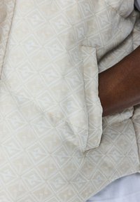 Beige gestreepte stof met geometrische vormen, met een detail van een zak en een zachte textuur. Het ontwerp is subtiel met lichte accenten.