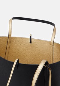 Sac cabas en cuir texturé noir et or avec deux anses en or et un dessus ouvert révélant la doublure intérieure dorée.