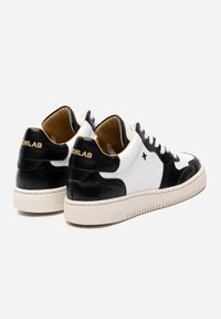 Sneakers in pelle bianca e nera con finitura testurizzata, colletto imbottito e suola in gomma beige. Accenti del logo dorato sul tallone.