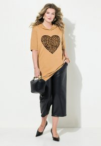 Tunic cappuccio marrone con un cuore a stampa leopardata, abbinata a culotte nere in ecopelle e tacchi a punta neri. Piccola borsa nera.