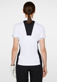 Vit polo t-shirt med svarta detaljer, korta ärmar och en slim fit. Har en svart panel på baksidan och märkesdetaljer på ärmarna.