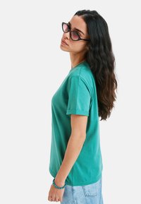 Turkis bomulds t-shirt med korte oprullede ærmer, rund halsudskæring og afslappet pasform, parret med lyse denimshorts.