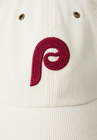 Hvit kordfløyelscaps med en teksturert, brodert burgunderlogo foran og messingeyelets for ventilasjon.