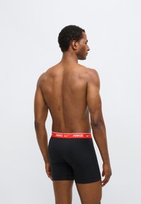 Fekete boxeralsó piros Nike logós derékpánttal. Az anyag simának tűnik, és testhezálló szabású. A kép hátulnézetet és oldalnézetet mutat.