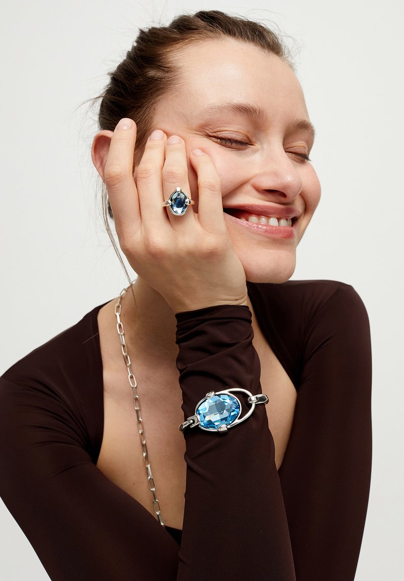 Anillo y pulsera de tono plateado con grandes piedras azules facetadas. Los suaves acentos metálicos contrastan con las superficies brillantes de las gemas.