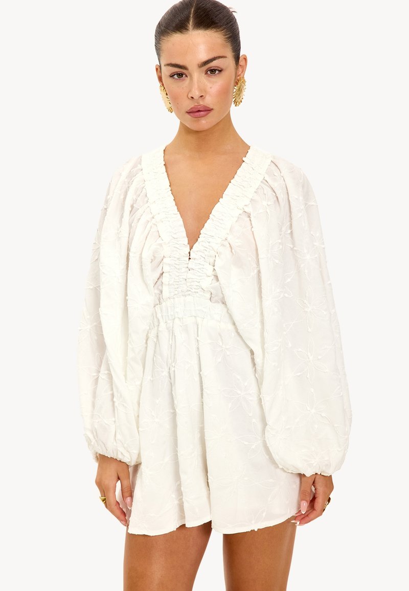 Witte geborduurde jurk met een diepe V-hals, elastische taille, volumineuze mouwen en een gestructureerd bloemenpatroon.