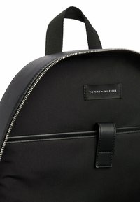 Zaino nero con una forma arrotondata, dotato di una cerniera argento, tessuto morbido, dettagli in pelle e un'etichetta con il marchio all'interno.