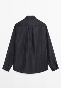 Chemise noire à manches longues avec un motif texturé subtil vue de dos, avec un col pointu et des poignets boutonnés.