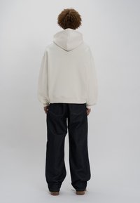 Blanding af bomuld, cremet hoodie med en stor hætte, parret med høj talje og løstsiddende mørke denim jeans med synlige baglommer.