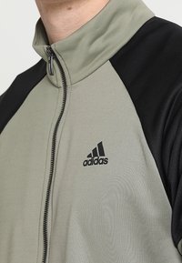 Gros plan d'une veste Adidas verte et noire avec un col zippé sur la partie supérieure du torse d'une personne.