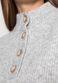 Hellgrauer, gerippter Pullover mit hohem Kragen und vier rundlichen Knöpfen in einem kontrastierenden Beige. Weiche Textur mit sichtbaren Strickmuster-Details.