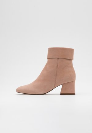 Bottine en daim rose avec un bout arrondi et un talon bloc. Elle présente un revers plié en haut et une texture lisse sur toute la surface.
