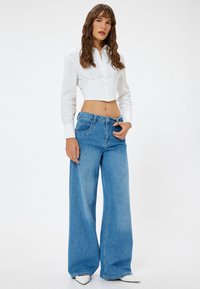Hvid kortærmet skjorte med lange ærmer og en struktureret krop, parret med løstsiddende blå denimjeans og spidse hvide hæle.
