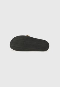 Black rubber shoe sole featuring a textured grip pattern, smooth edges, and a slight upward curve at the toe with gold accent hardware.