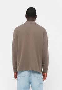 Brown long-sleeve polo with a relaxed fit, featuring a classic collar and ribbed cuffs, paired with light blue baggy denim jeans.