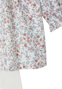 Weiße Stoff mit kleinen rosa und gelben Blüten sowie grünen Blättern, zeigt einen Teil eines Langarmkleidungsstücks und weißer Hose.